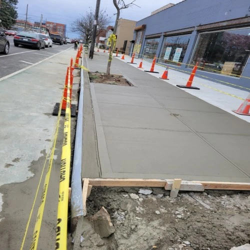 A sidewalk is being constructed in front of a building by concrete contractors.